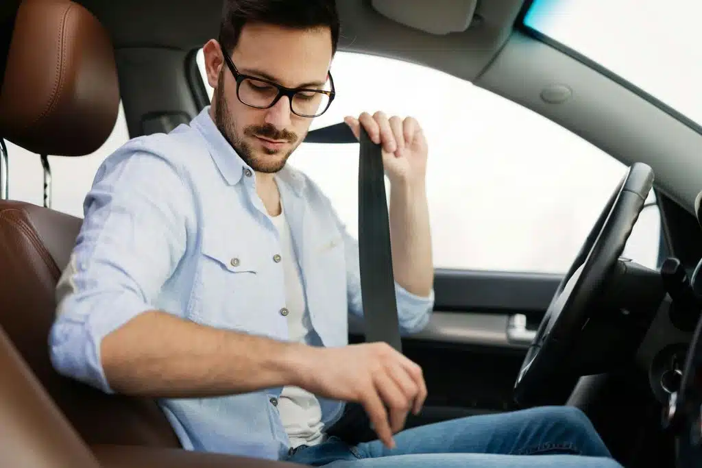 A person buckles their seatbelt in the driver's seat of a car.