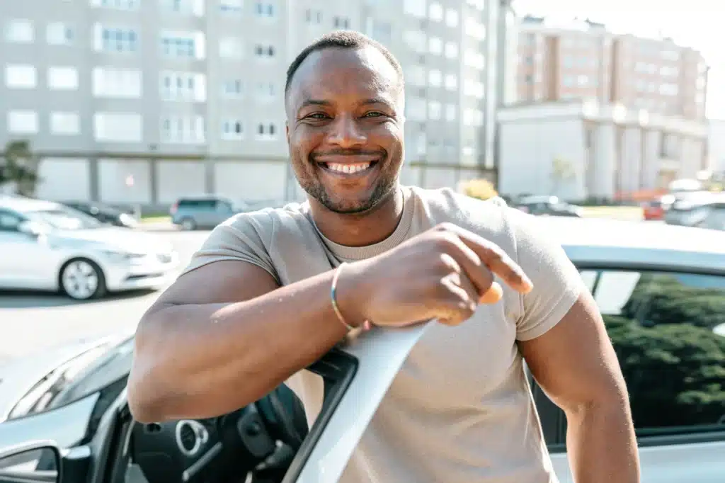 A person leans on their car door and smiles after calling a traffic ticket expert and getting their charges dismissed.