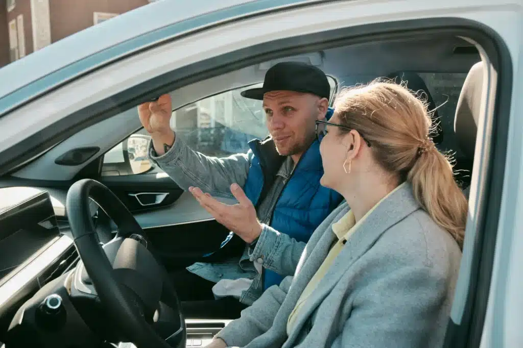 A person in the passenger seat of a car adjusts the rearview mirror to help the driver avoid hitting another car parked behind them.