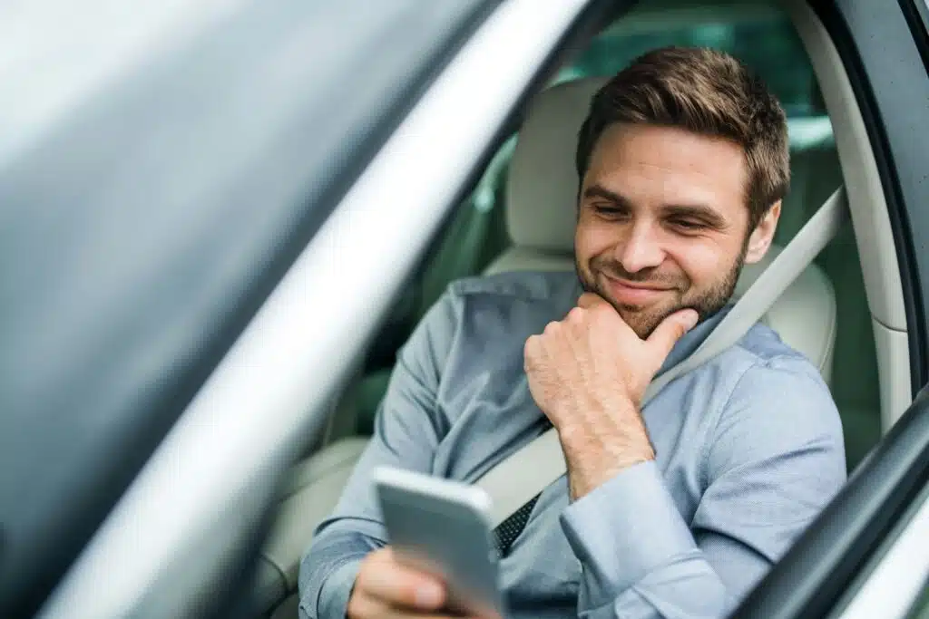 A person in the driver's seat of a car smiles while looking at their phone, calling a traffic ticket fighter in Calgary.