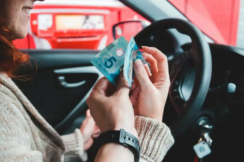 A driver with money in hand smiles thinking of the money they saved by on traffic ticket fines in Alberta.
